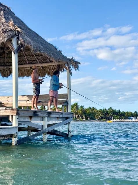 Guests fishing from the pier beneath the thatched palapa