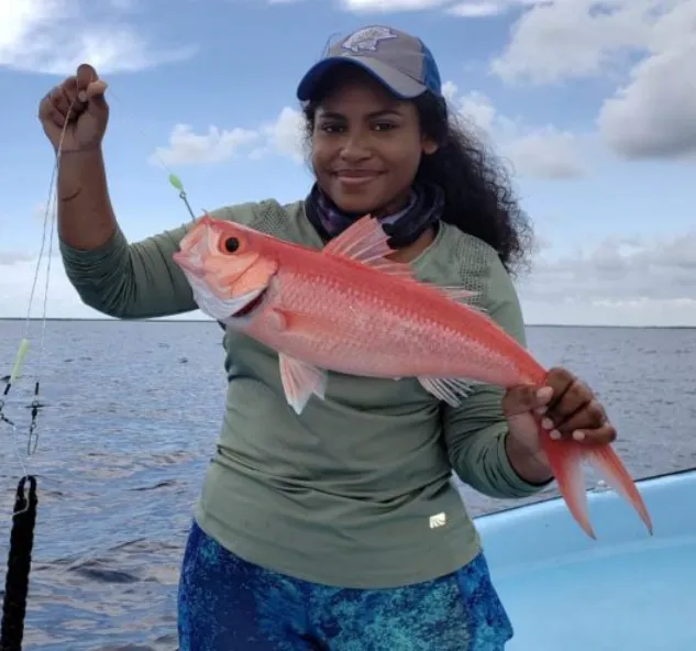 A smiling angler holding up a bright red snapper on a boat