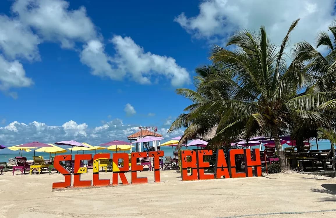 Red Secret Beach letters on the sand, with colorful umbrellas and palms behind