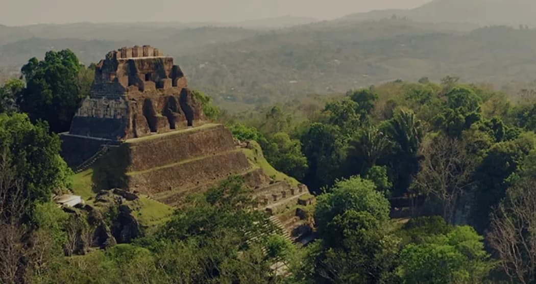 A Maya pyramid rising above the jungle canopy under a hazy sky