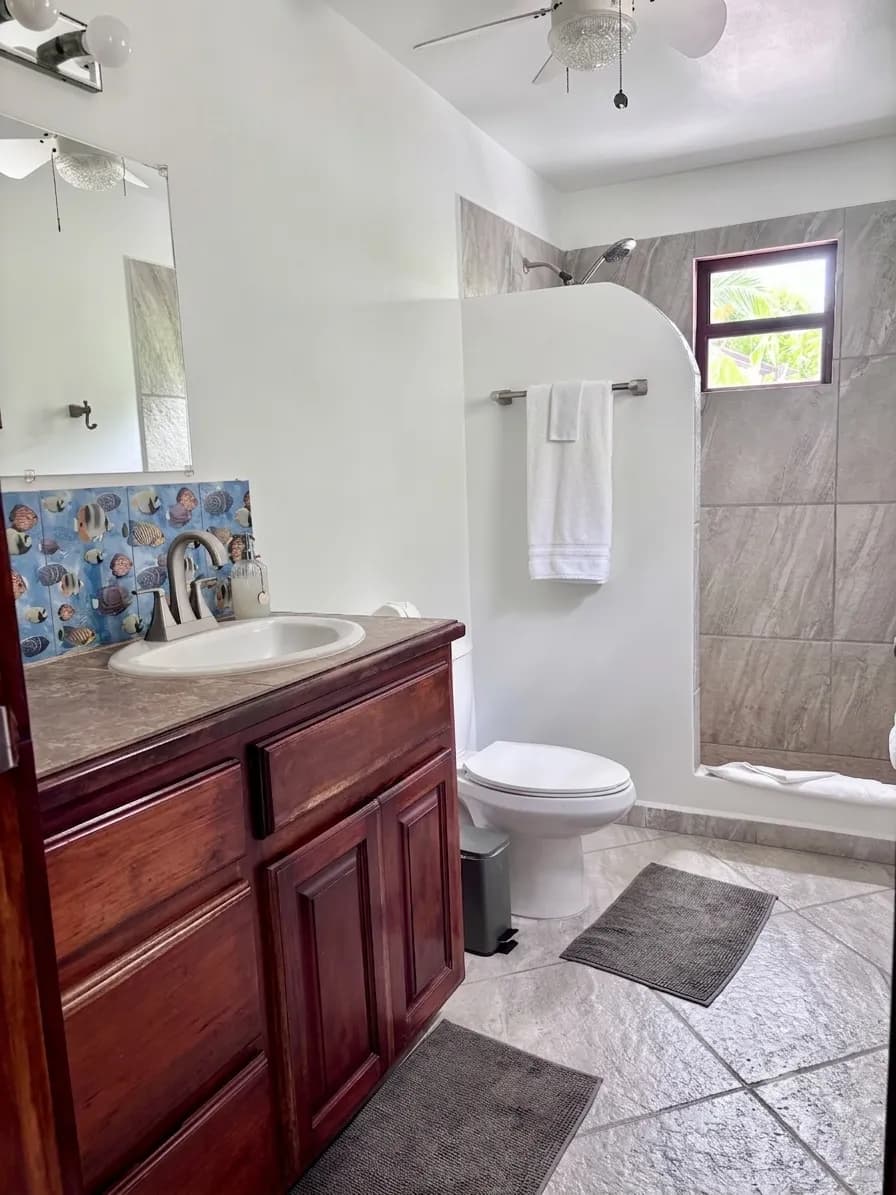 A bathroom with a wood vanity, a colourful tile splashback and a tiled shower