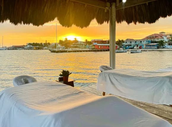 Two massage tables under a thatched roof facing the sea at sunset