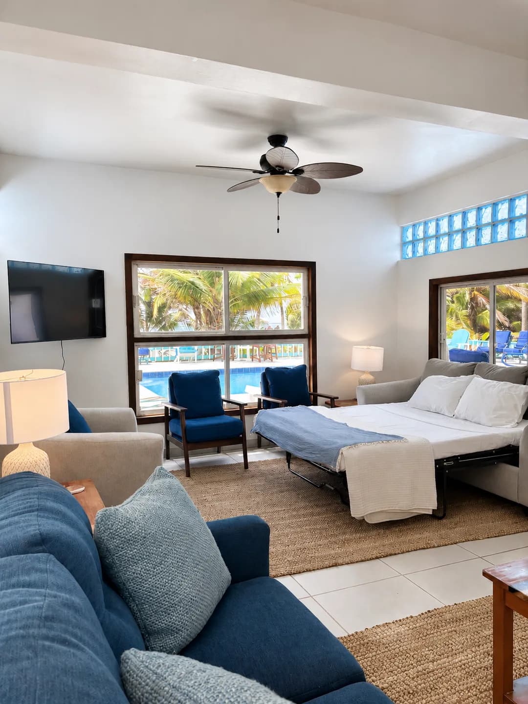 The living room with its sofa pulled out into a made-up bed, facing windows onto the pool