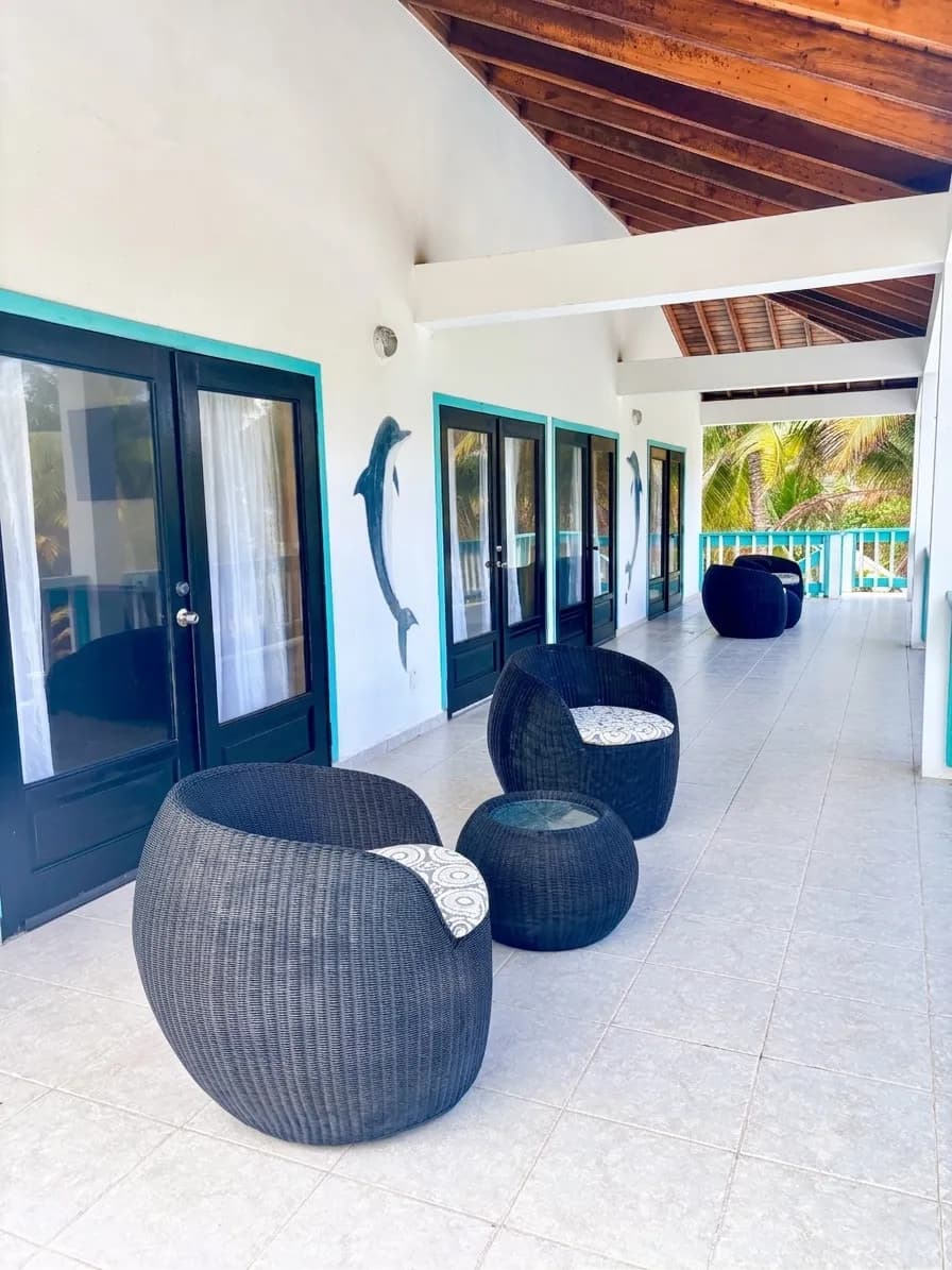 A tiled veranda with woven chairs, turquoise railings and a dolphin sculpture on the wall